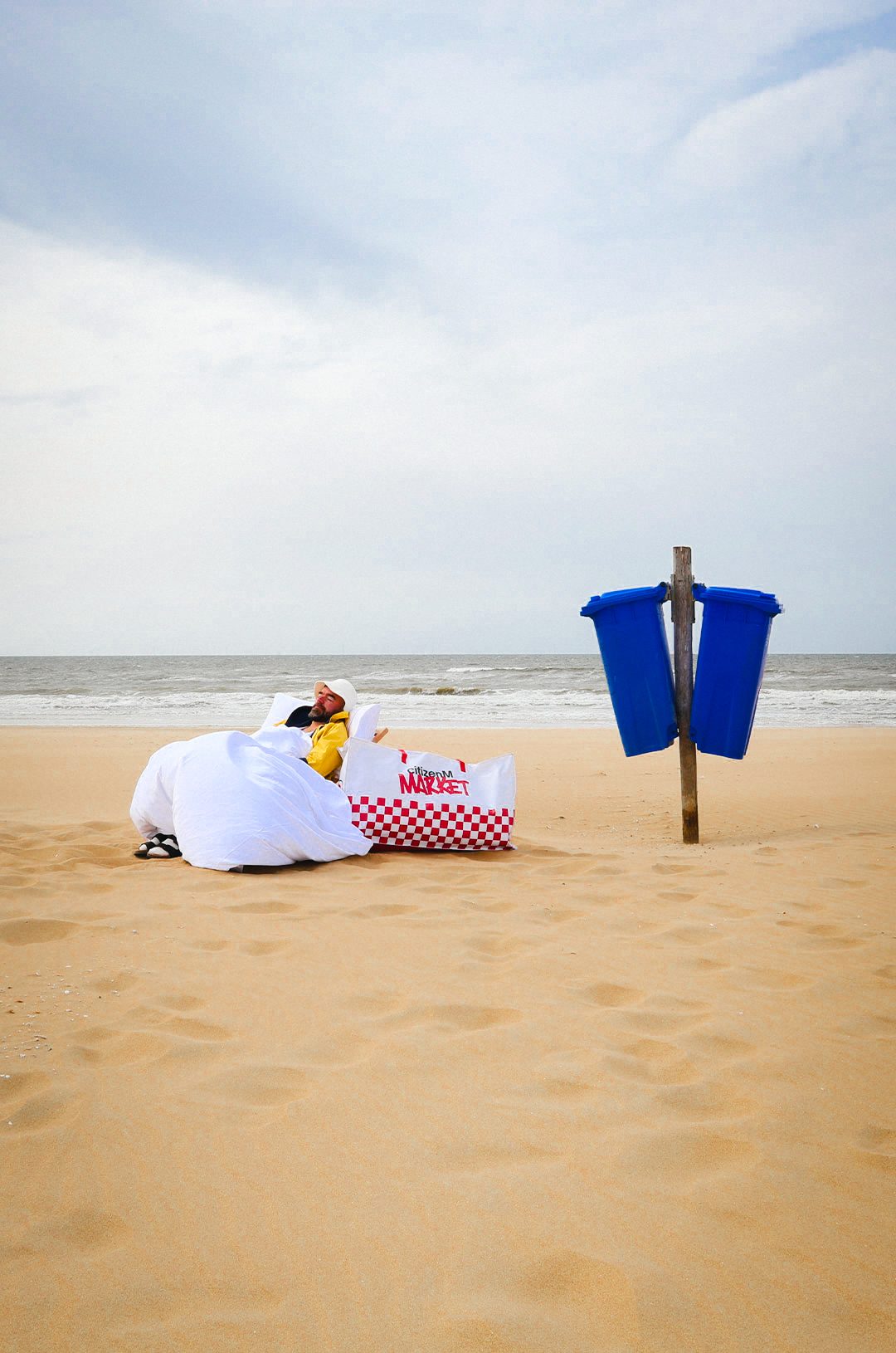 A bed made up on the beach next to a blue bin