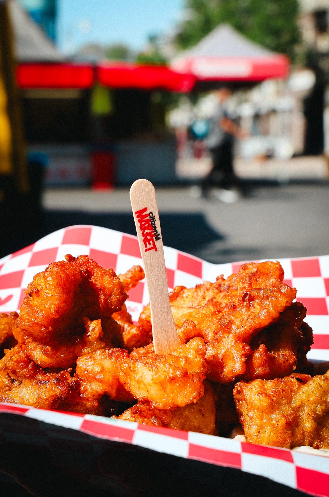 Fried snack in a red and white checked tray with a .market wooden fork