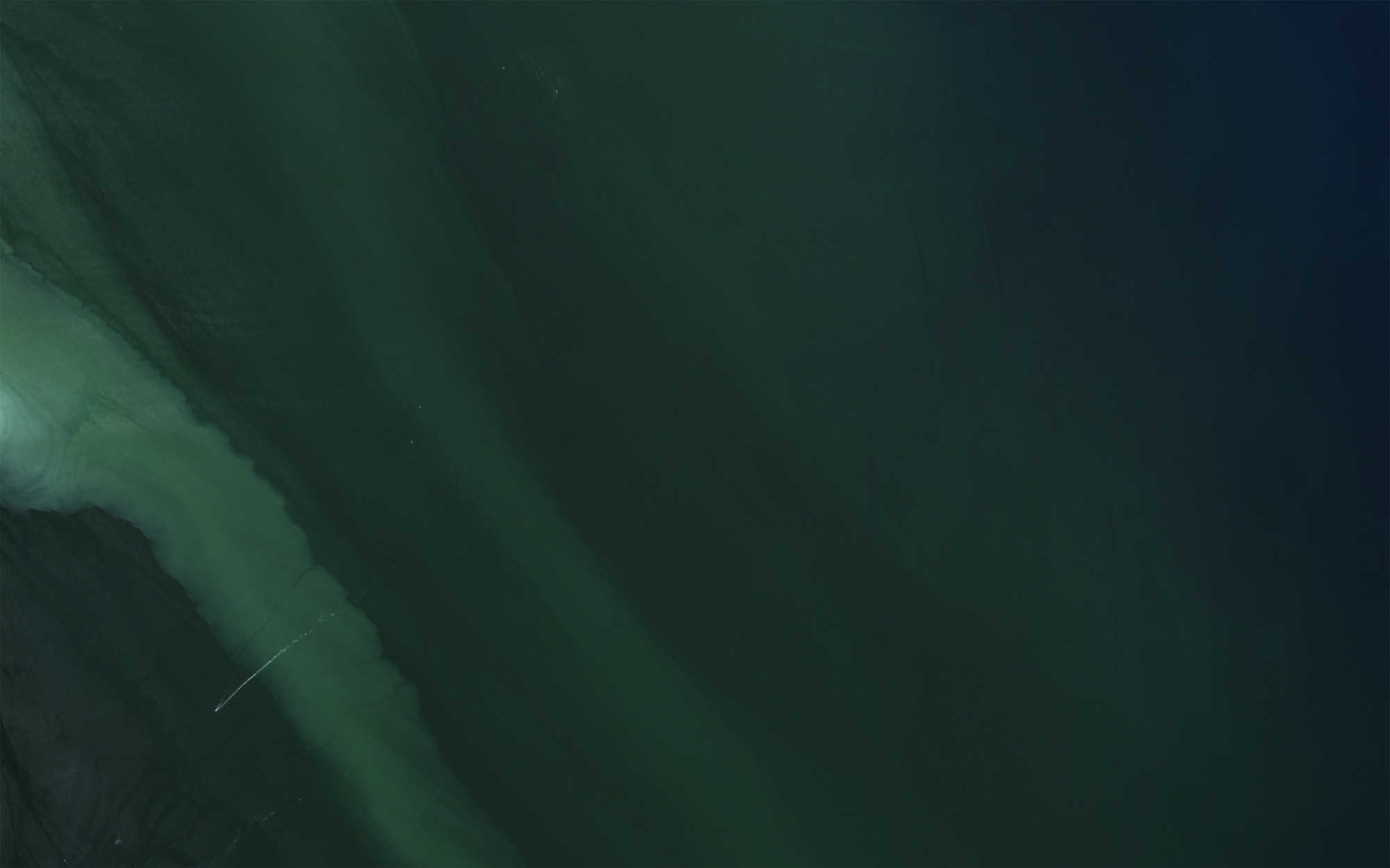 A pale band of sediment curving through dark green water