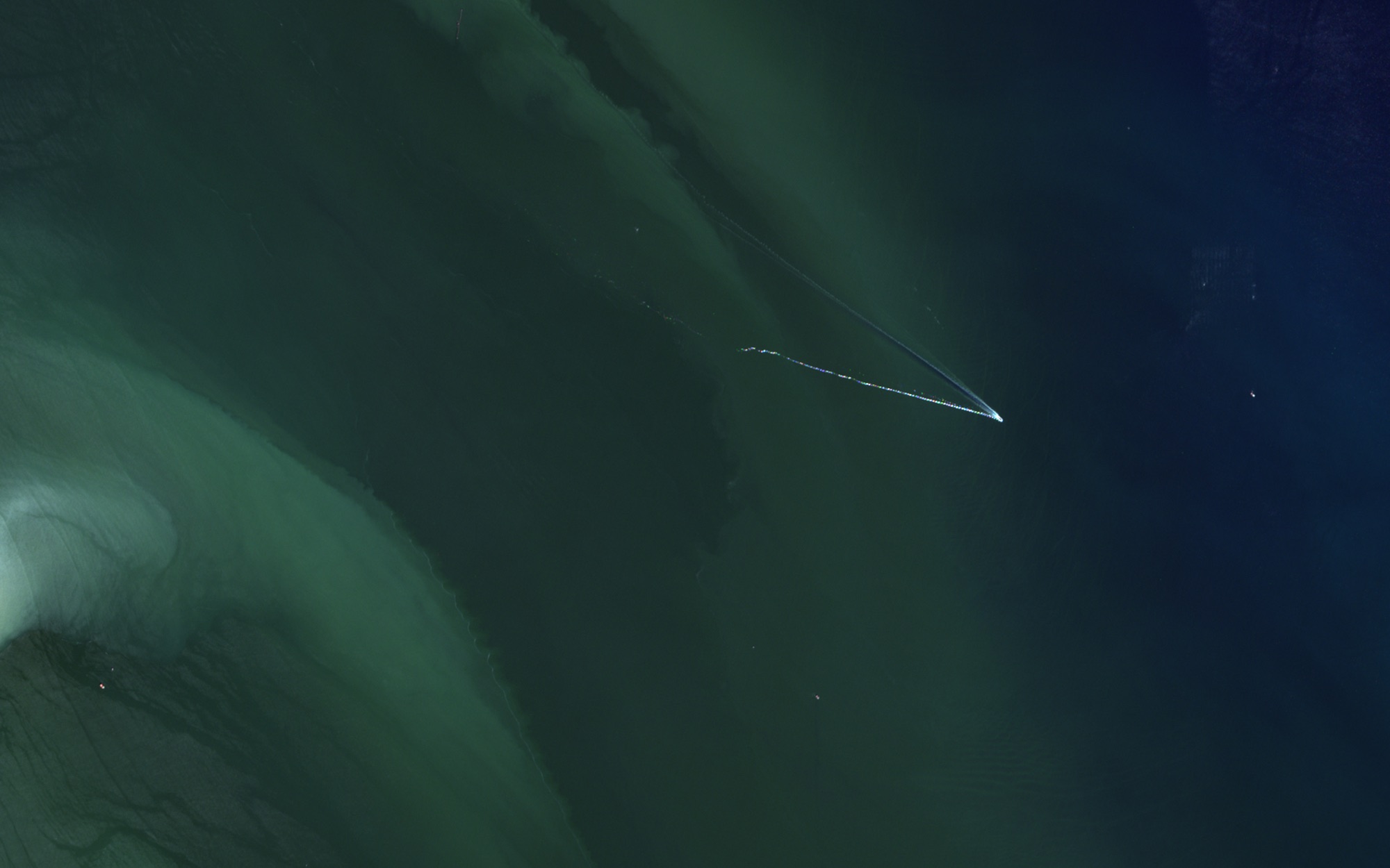 A boat's wake cutting across bands of green sediment
