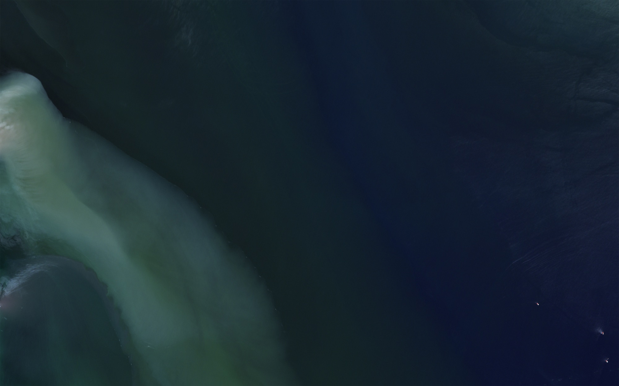 A plume of pale sediment turning into dark blue water